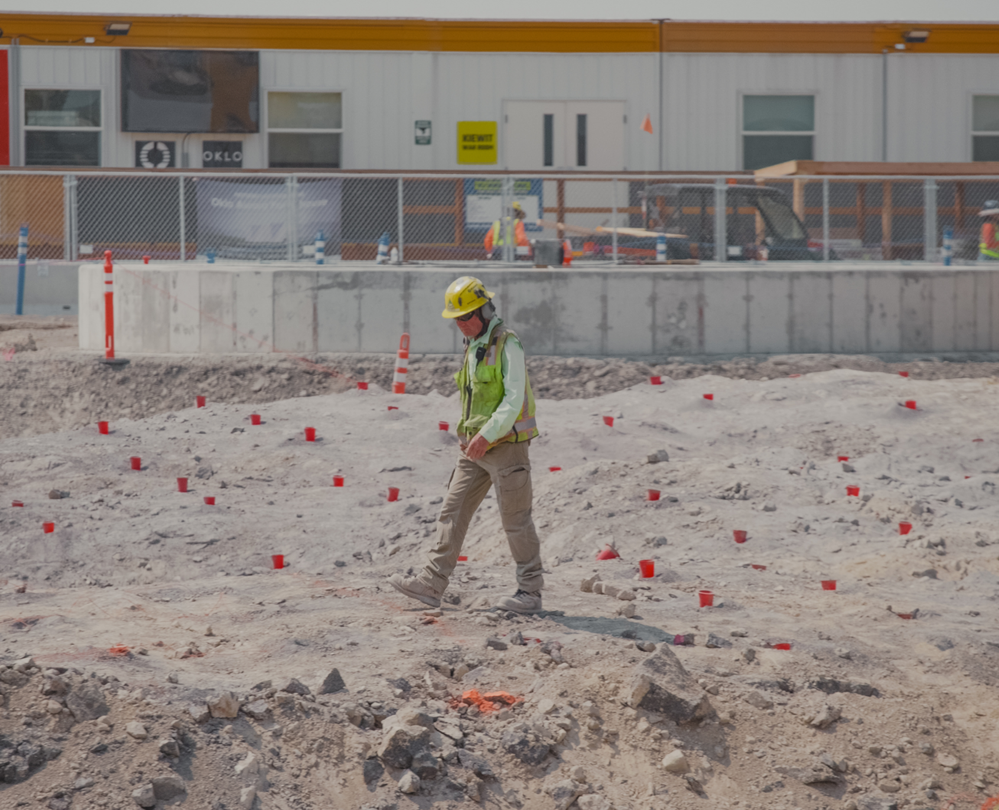 Worker in high-visibility gear walking a flagged construction path