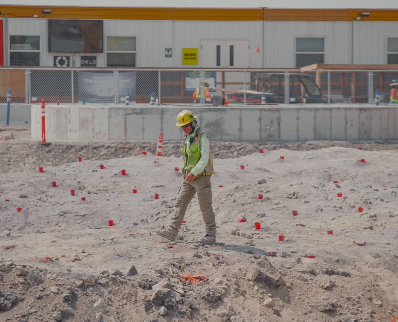 Worker in high-visibility gear walking a flagged construction path