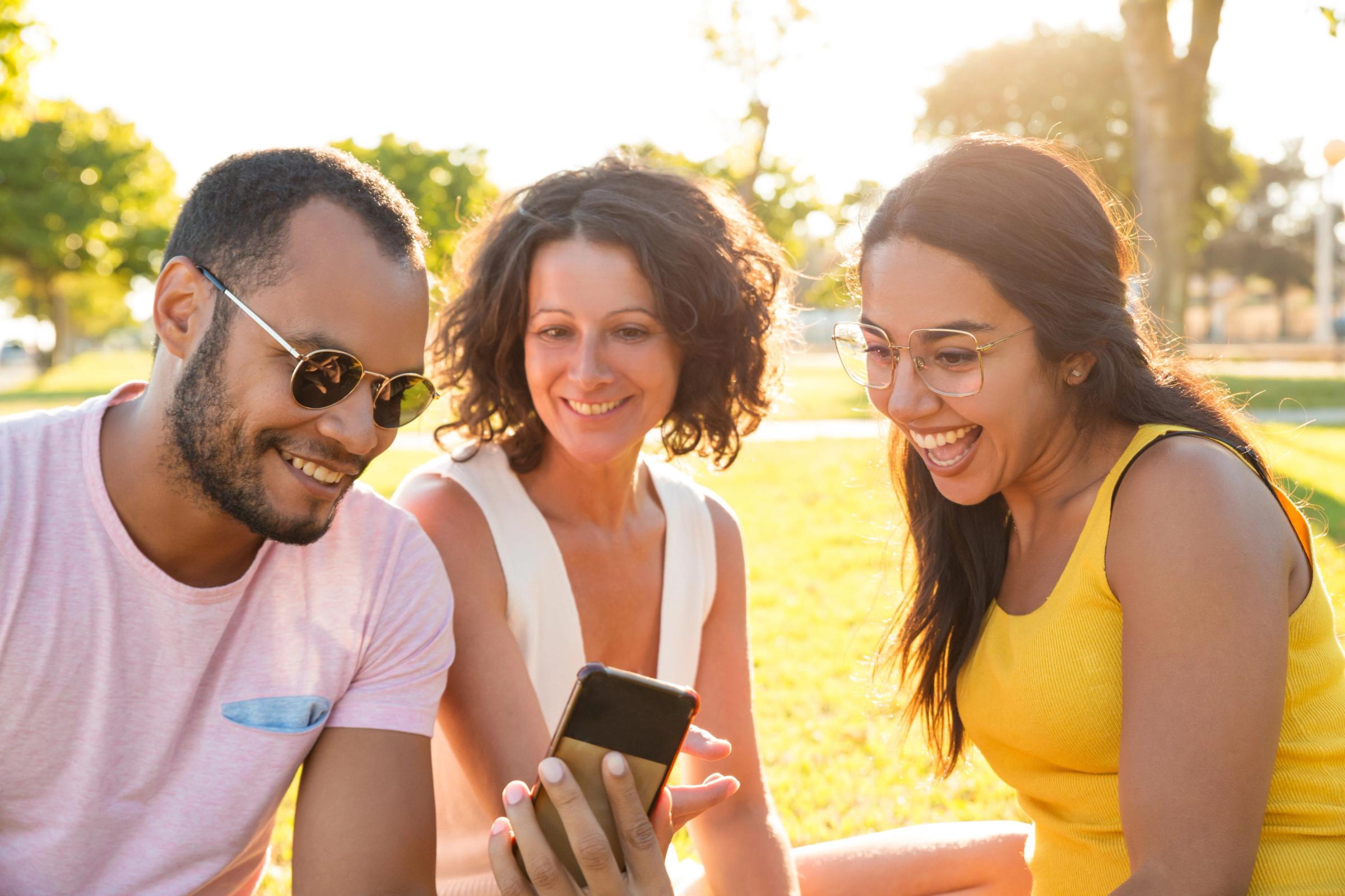 Three friends smiling and looking at a phone in a park