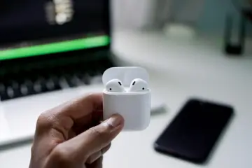 Ruka držící sluchátka AirPods před notebookem MacBook