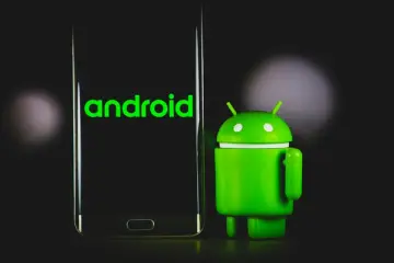 Android maskot stojící vedle smartphonu se zeleným logem Androidu na obrazovce.