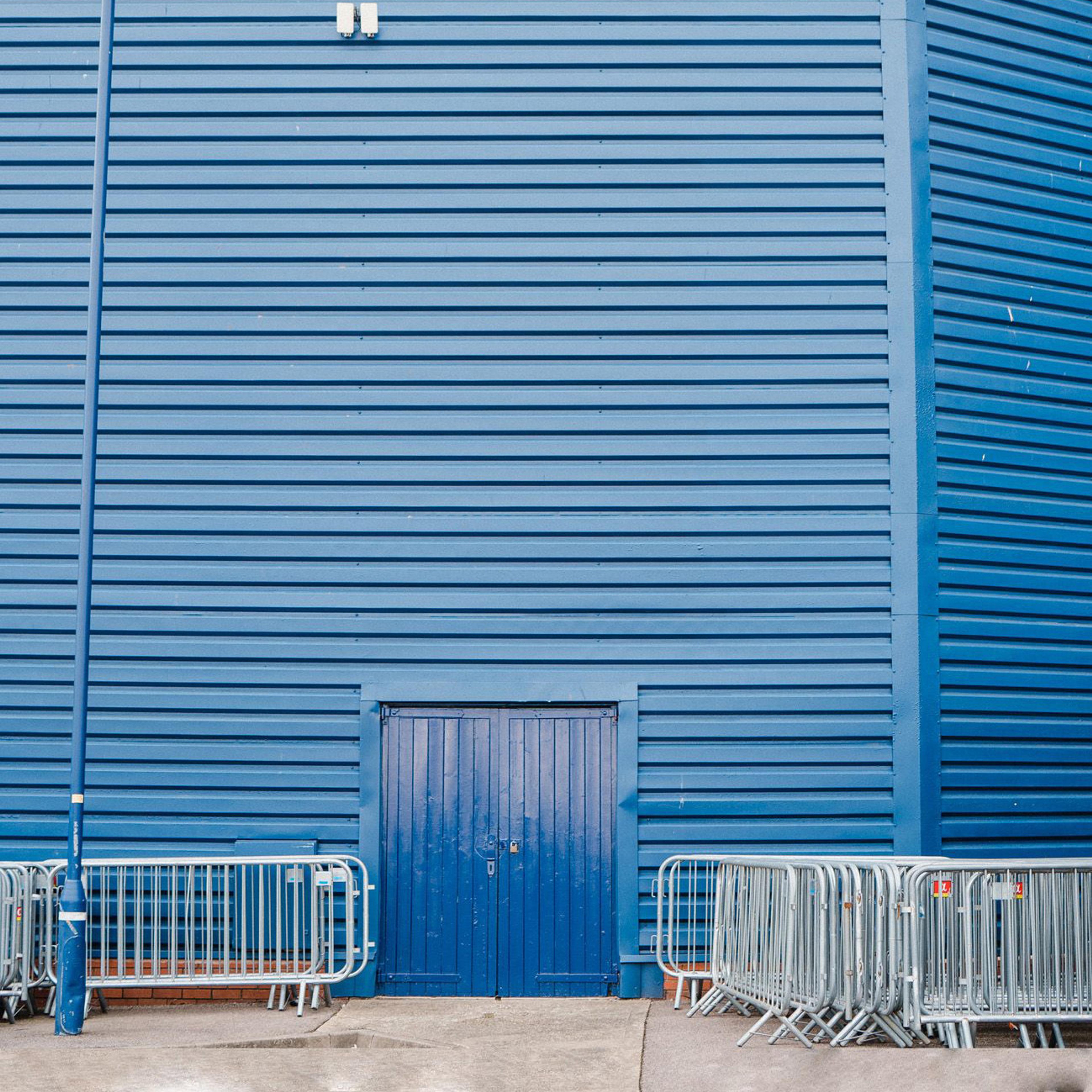 Some security fences stacked up next to a padlocked entrance to a tall blue building