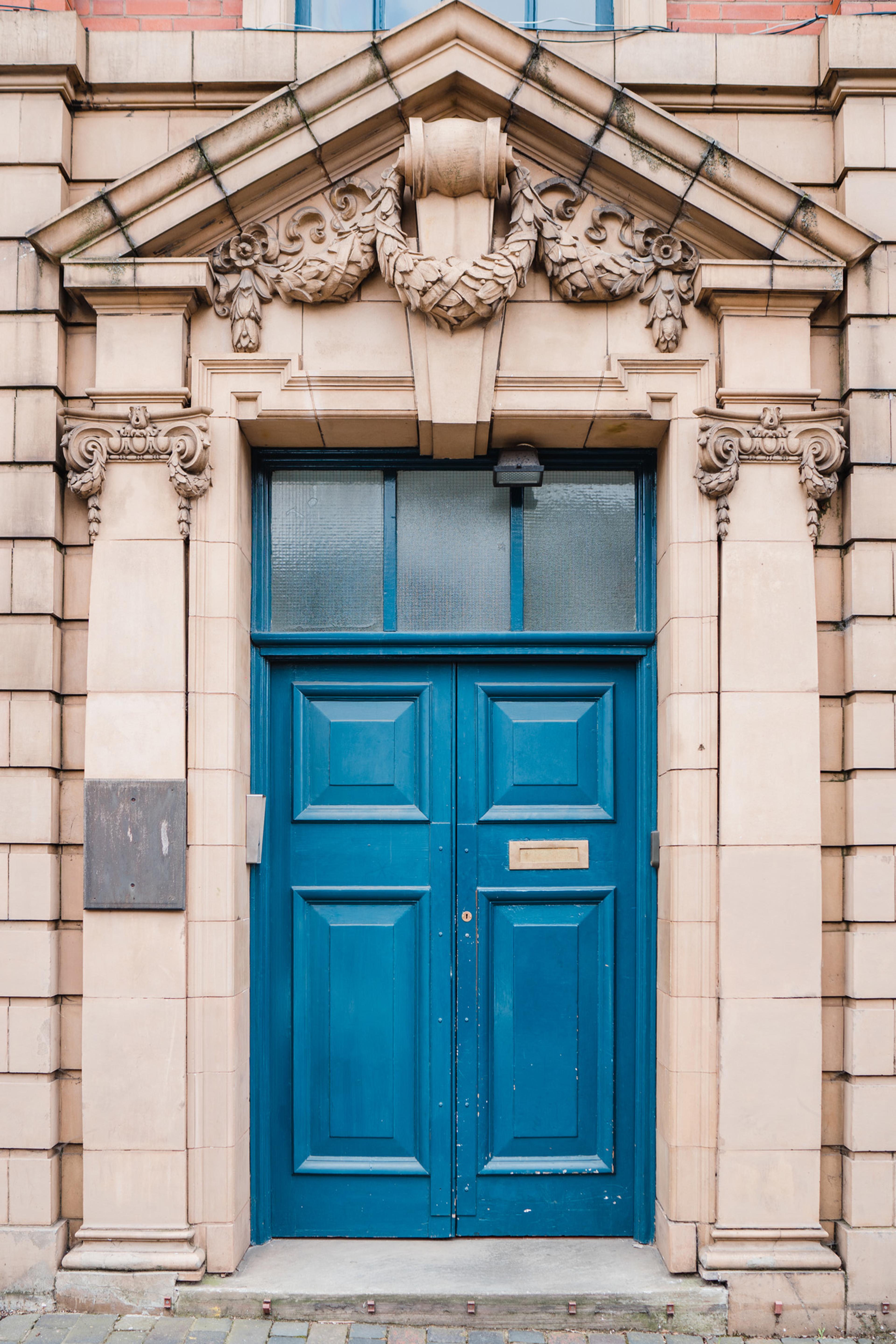 A blue double door with brass letterbox under an ornate facade