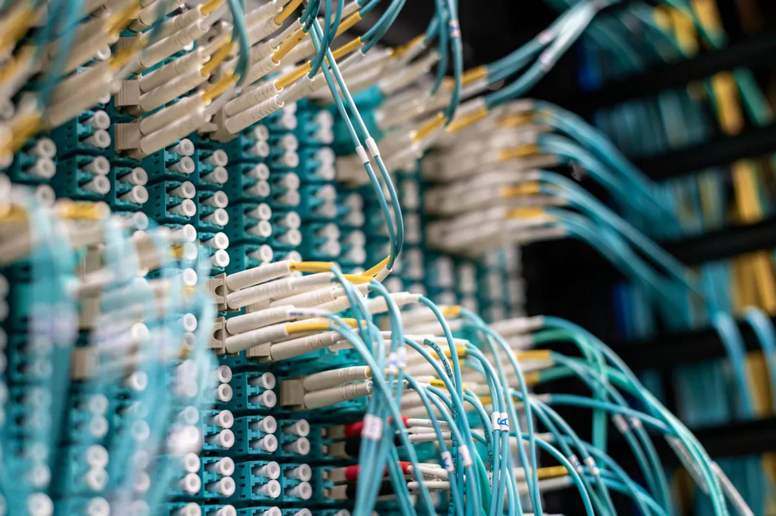 Bir veri merkezinde kabinlere takılı çok sayıda turkuaz fiber optik kablo ve beyaz konnektörler