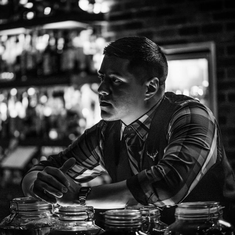A Rock and Rye bartender leaning on the bar, in black and white