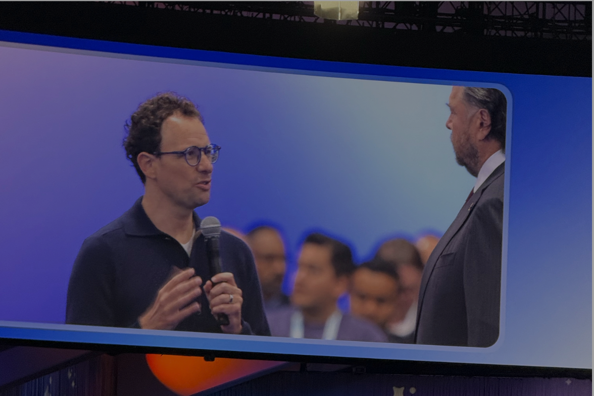 Anthropic CEO Dario Amodei speaking into a microphone while conversing with Salesforce CEO Marc Benioff on a large event screen at Dreamforce