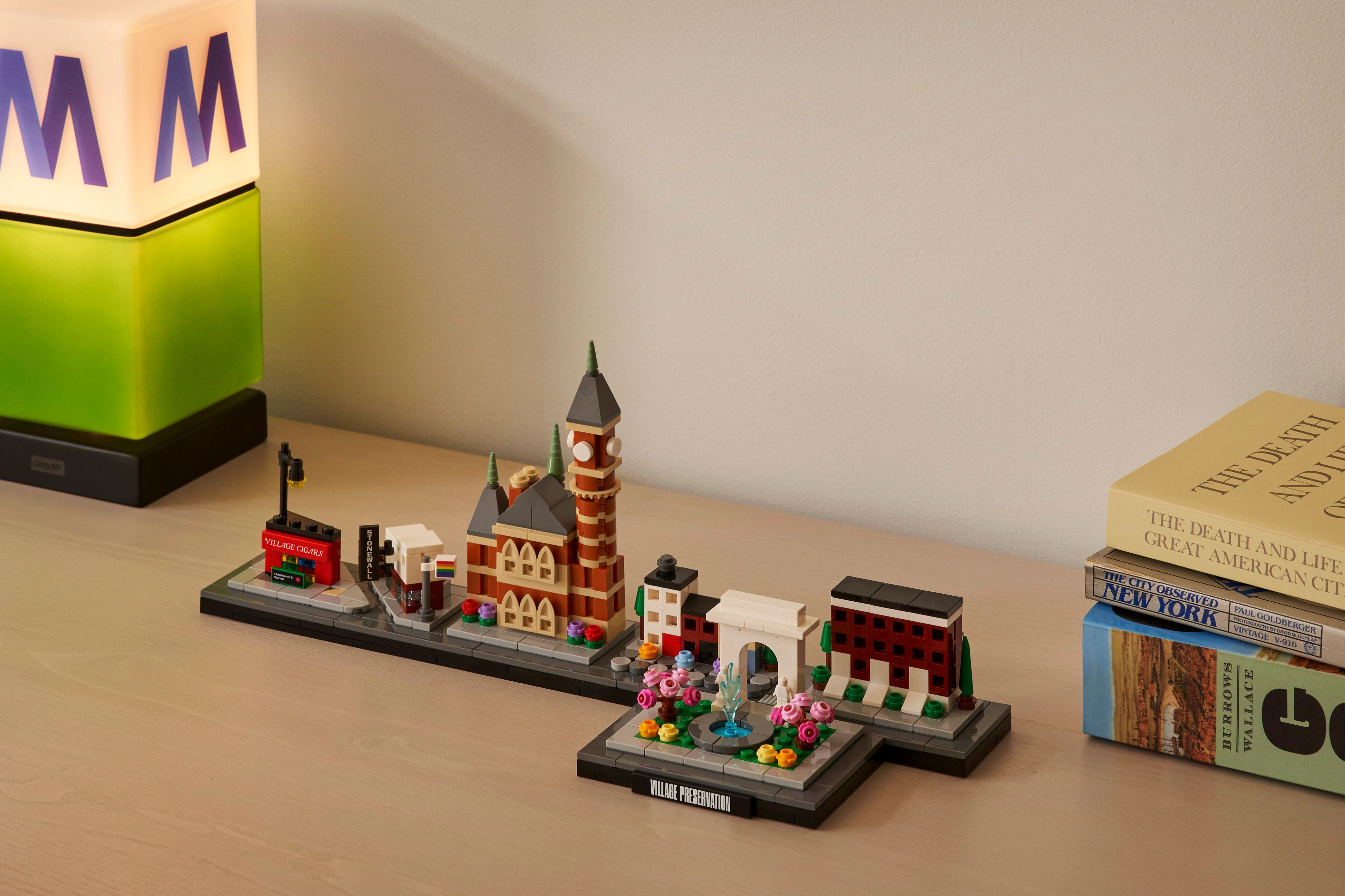 A color photograph of the Greenwich Village Building Set sitting on a table next to books and a lamp.