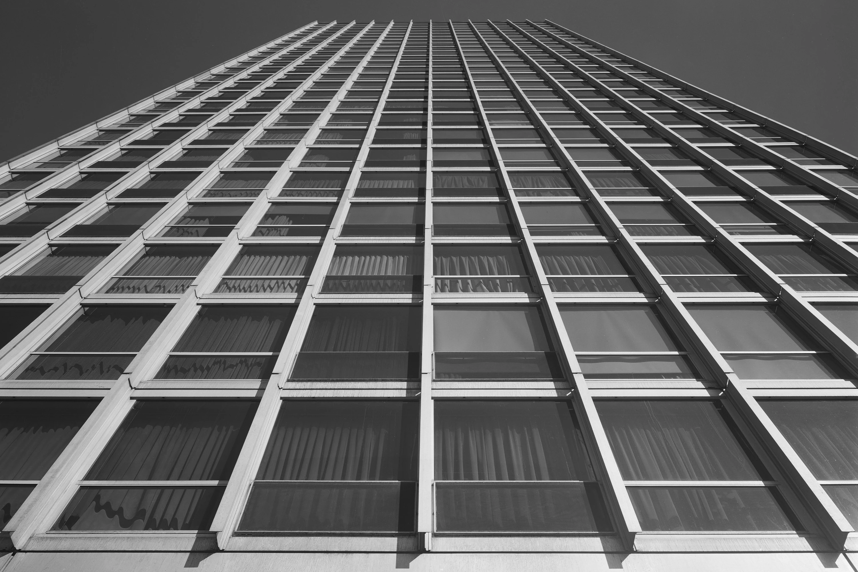 A black-and-white photograph of a modern skyscraper, viewed from below looking upwards.