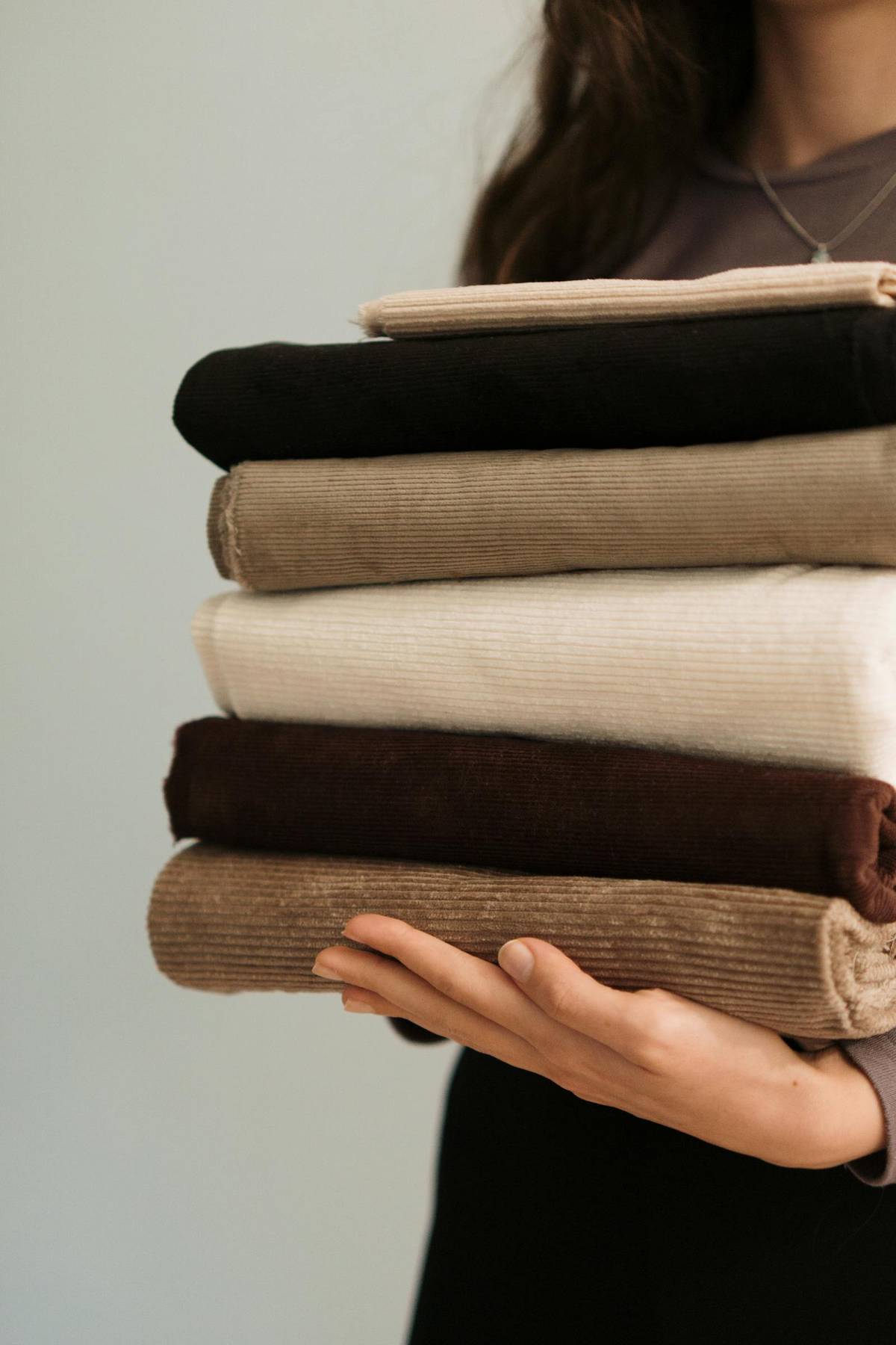 A person holding a stack of folded fabrics in warm neutral tones.