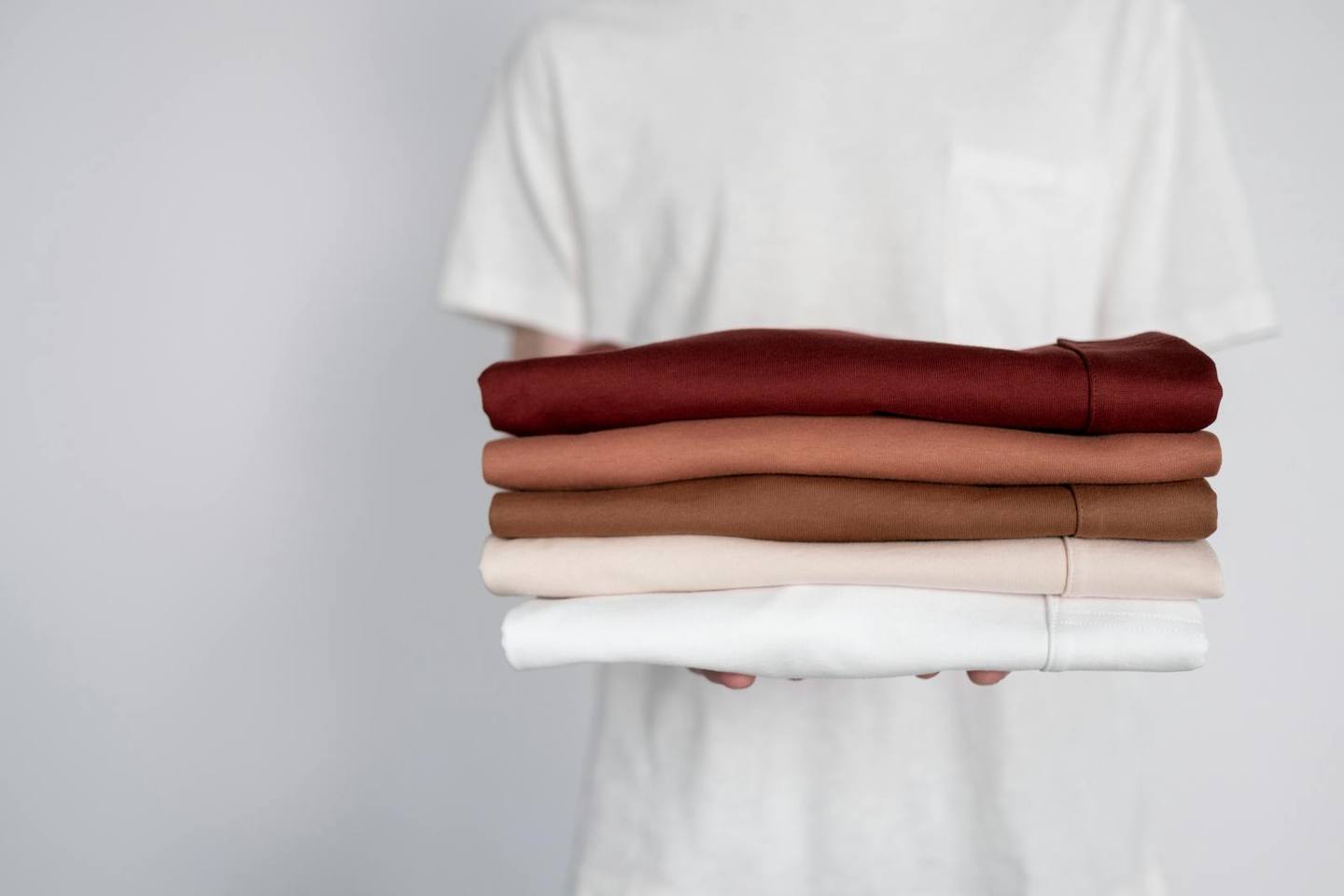 A person holding neatly folded textile pieces in earthy tones against a clean background.