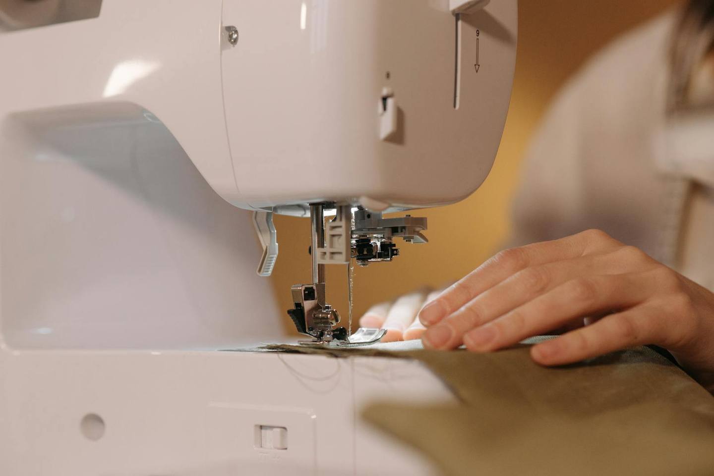 Hands guiding fabric through a sewing machine in warm studio light.