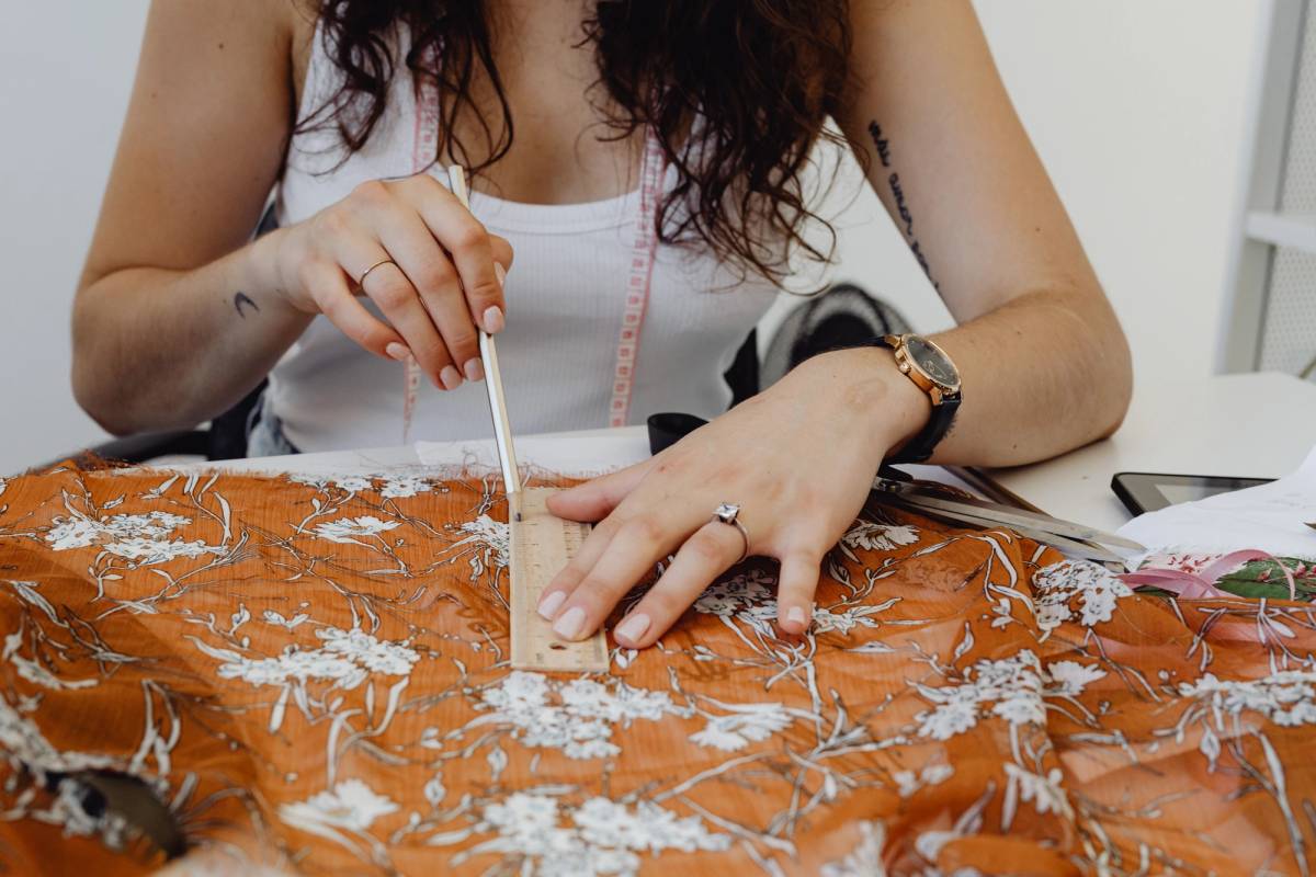 Designer measuring patterned fabric with a ruler at a worktable before production