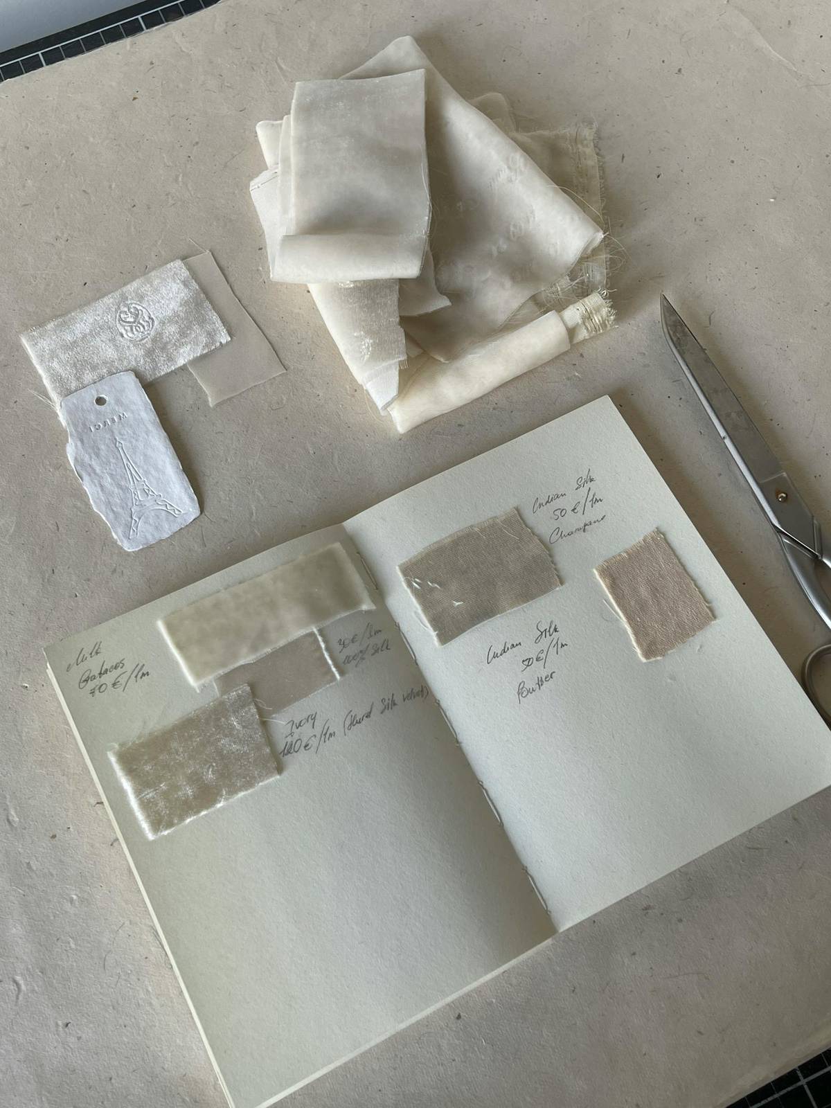 Fabric swatches, notes, and tools arranged on a desk for early-stage sourcing decisions.