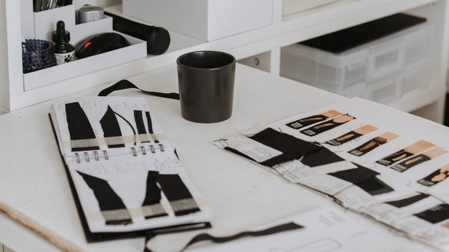 Fashion design worktable with garment sketches, fabric swatches, and label samples