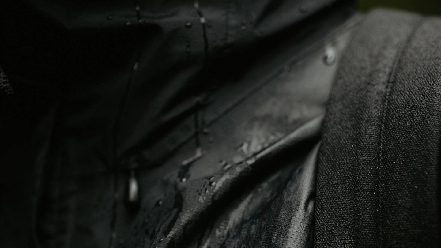 Close-up of dark water-repellent textile with rain droplets and visible woven texture