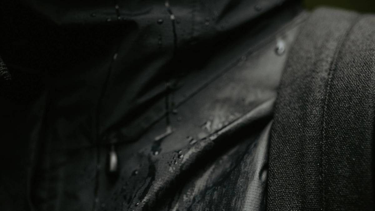 Close-up of dark water-repellent textile with rain droplets and visible woven texture