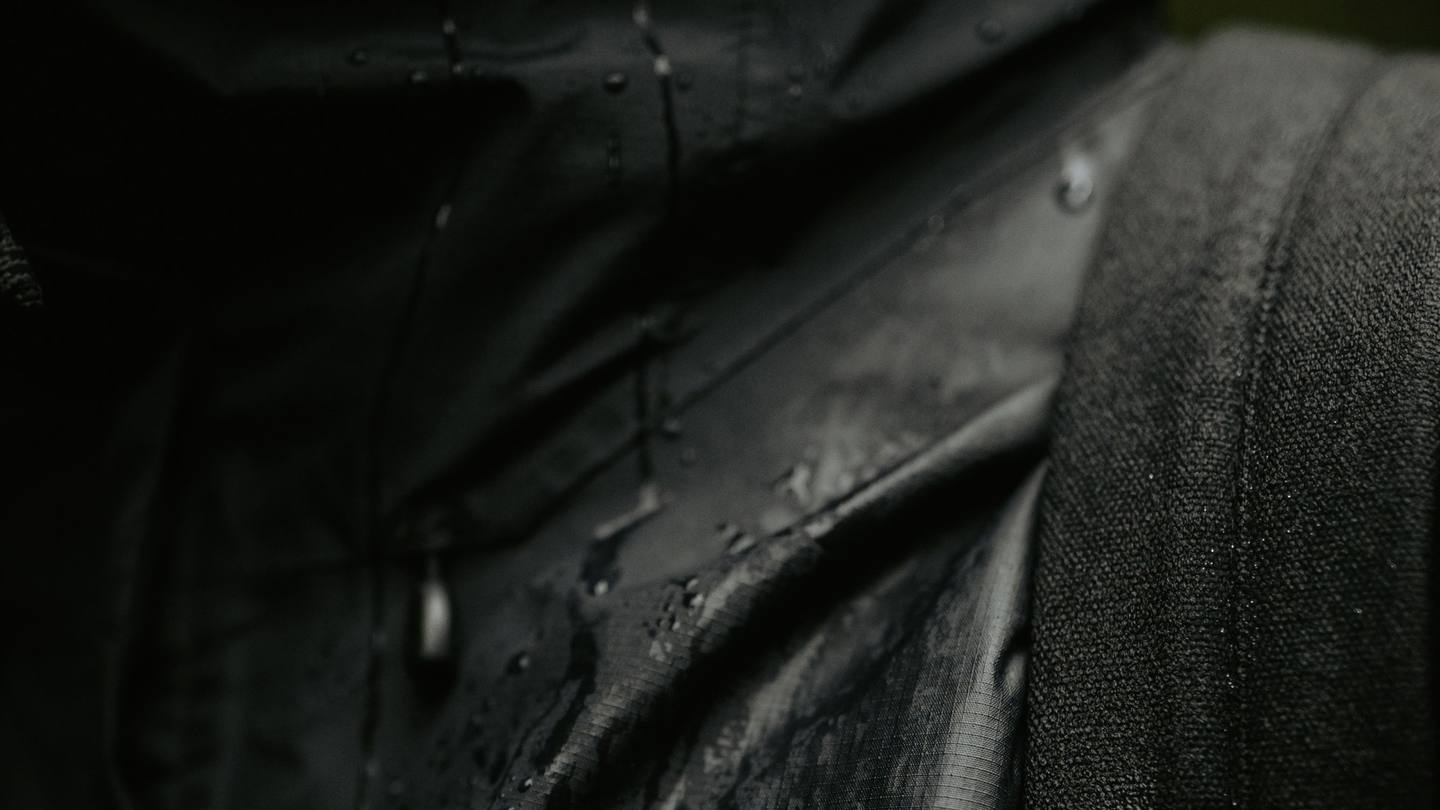 Close-up of dark water-repellent textile with rain droplets and visible woven texture