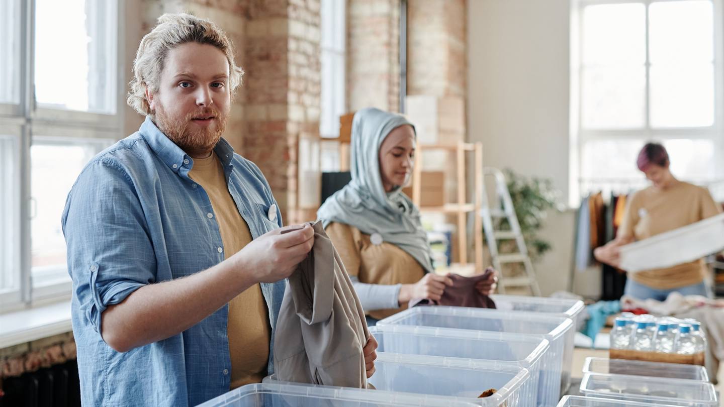 People sorting used clothing into clear collection bins in a bright community workspace