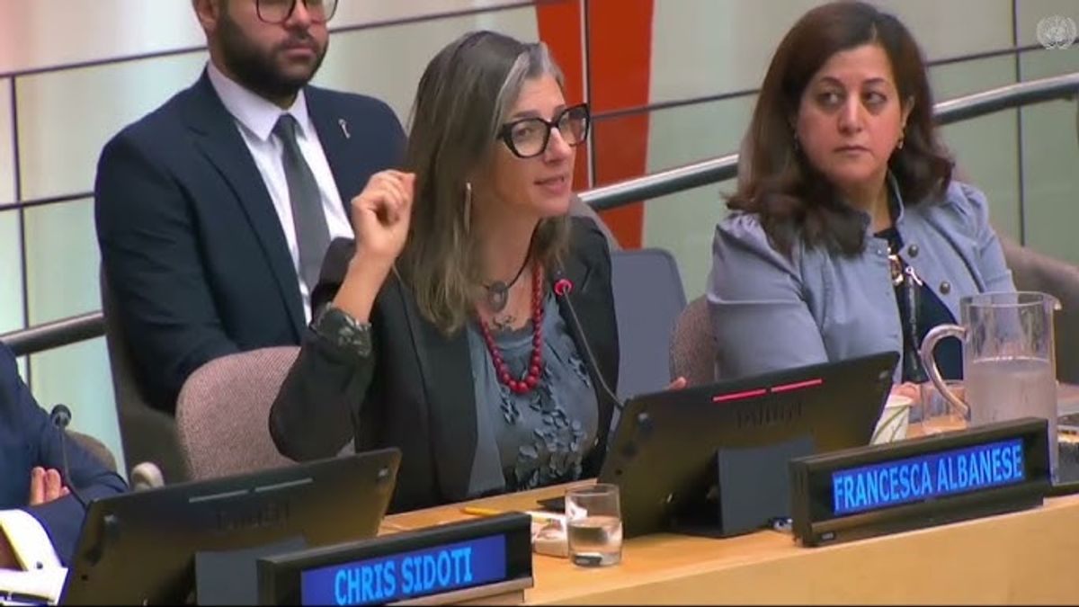 A woman sitting on a panel speaks into the mic at a meeting and gestures with her hand. 