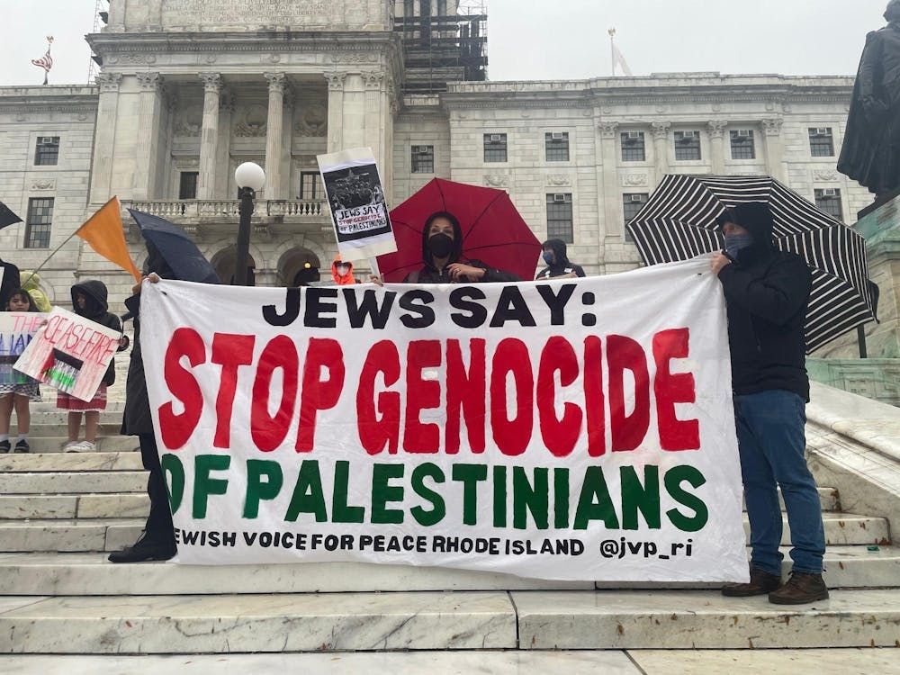 A group of people stand at the steps of the State House with a banner that reads "Jews say: stop genocide of Palestinians".