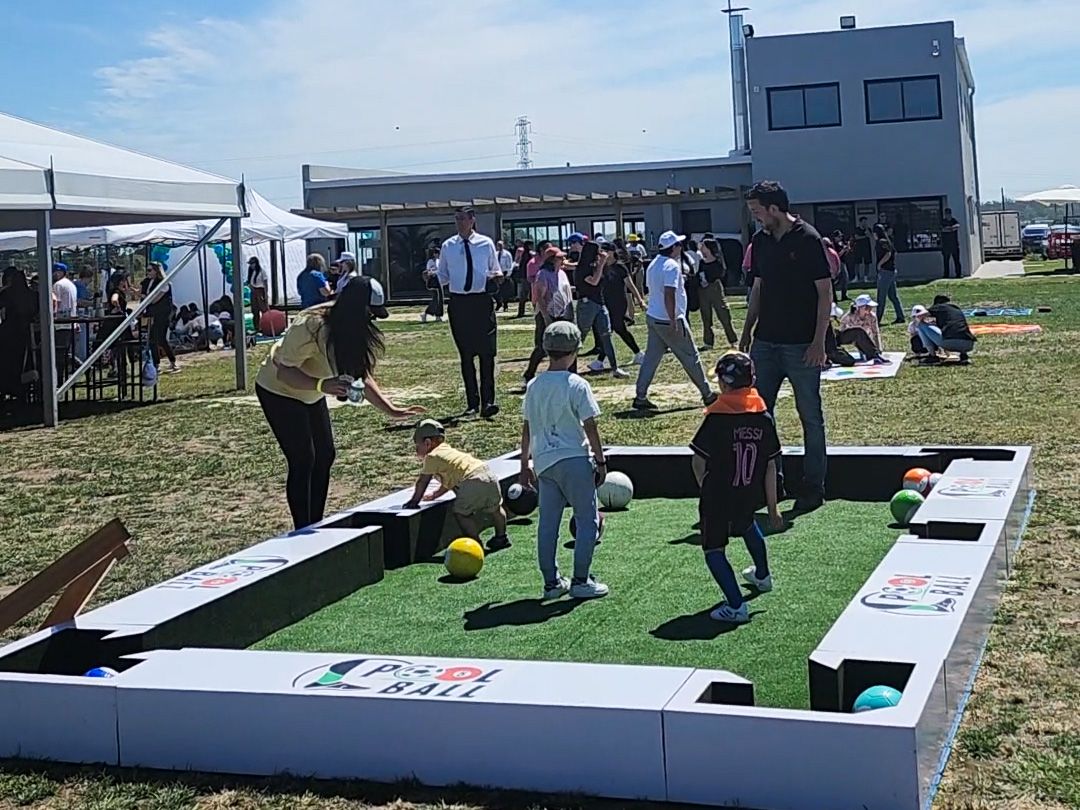 Chicos y grandes juegan al pool con pelotas de fútbol sobre una mesa gigante de pasto sintético, al aire libre