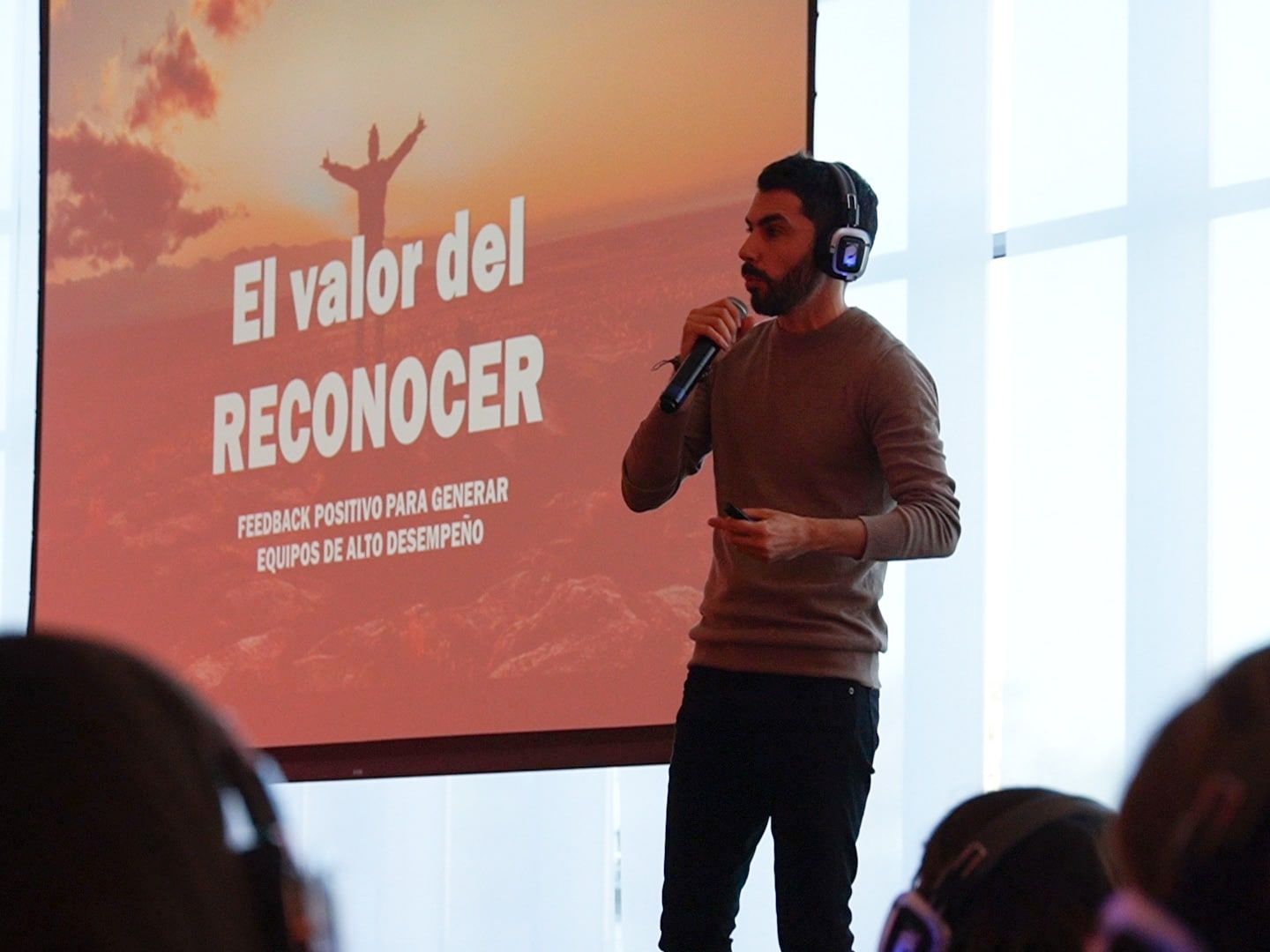 Un orador con micrófono presenta «El valor del reconocer» frente a la pantalla