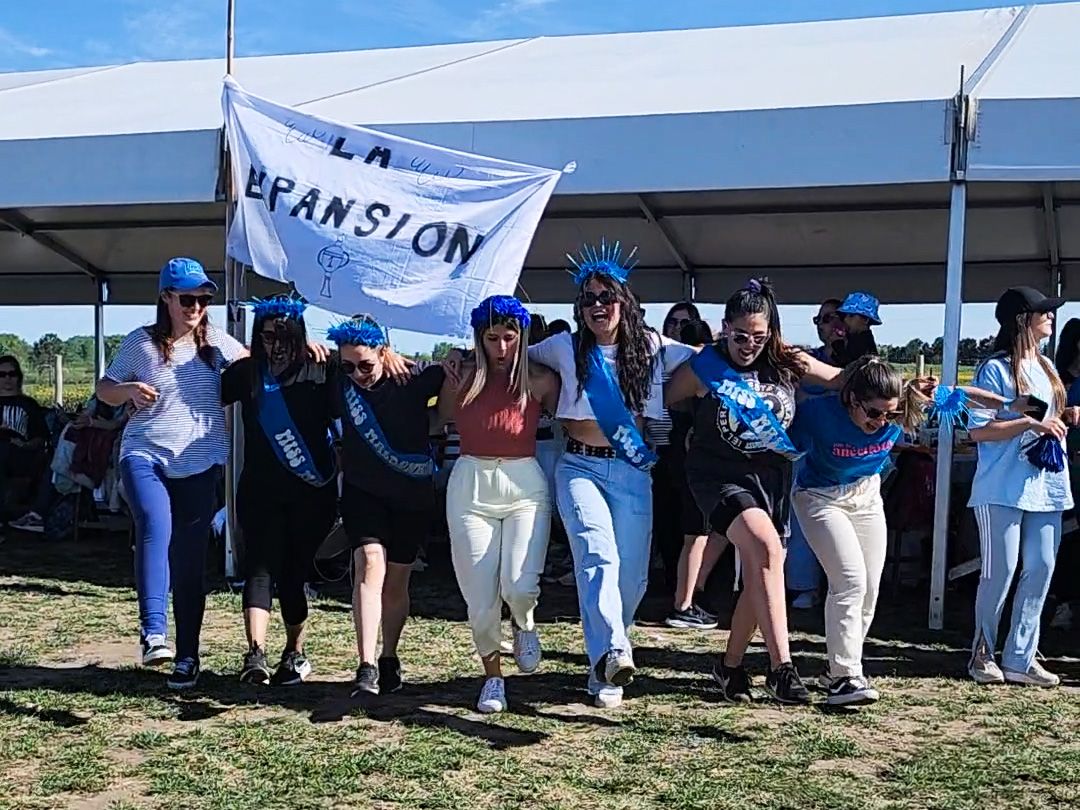 Un equipo con gorros y bandas celestes posa abrazado bajo una carpa, con su bandera