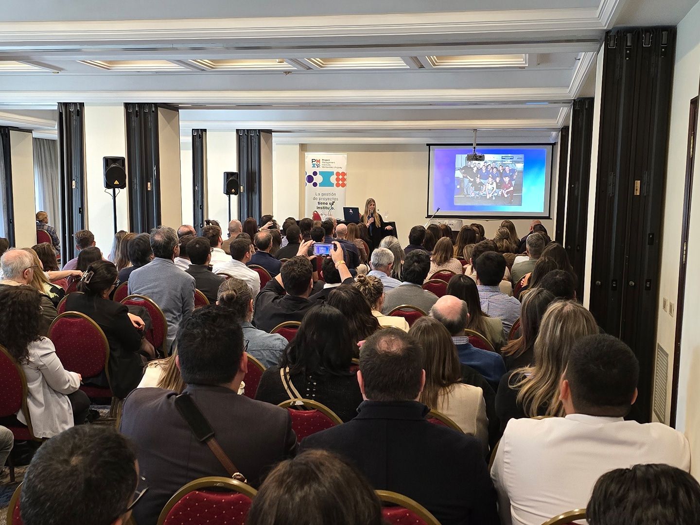 Público sentado en el salón mira una presentación proyectada en el escenario