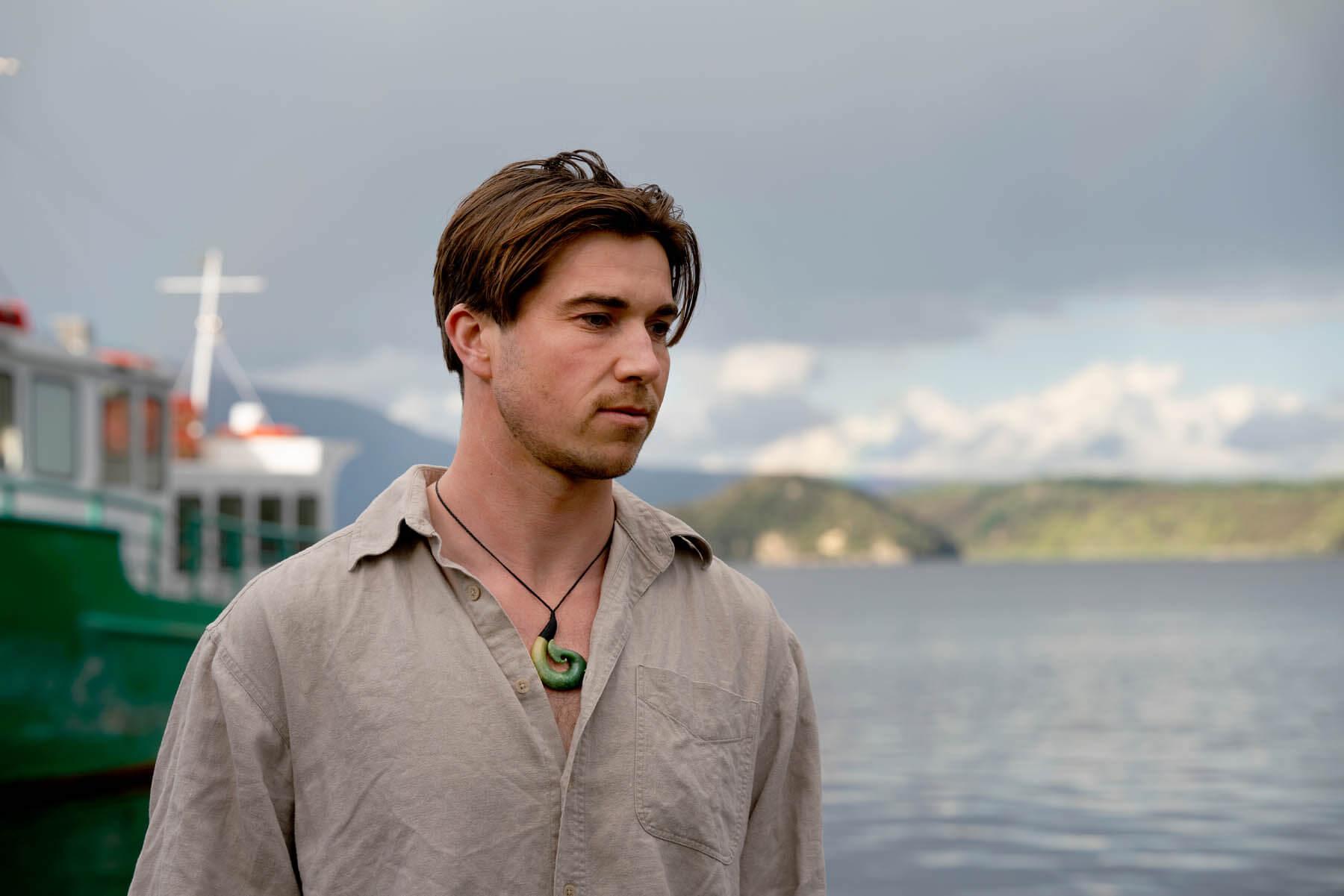 Man wearing hei matau with boat in background