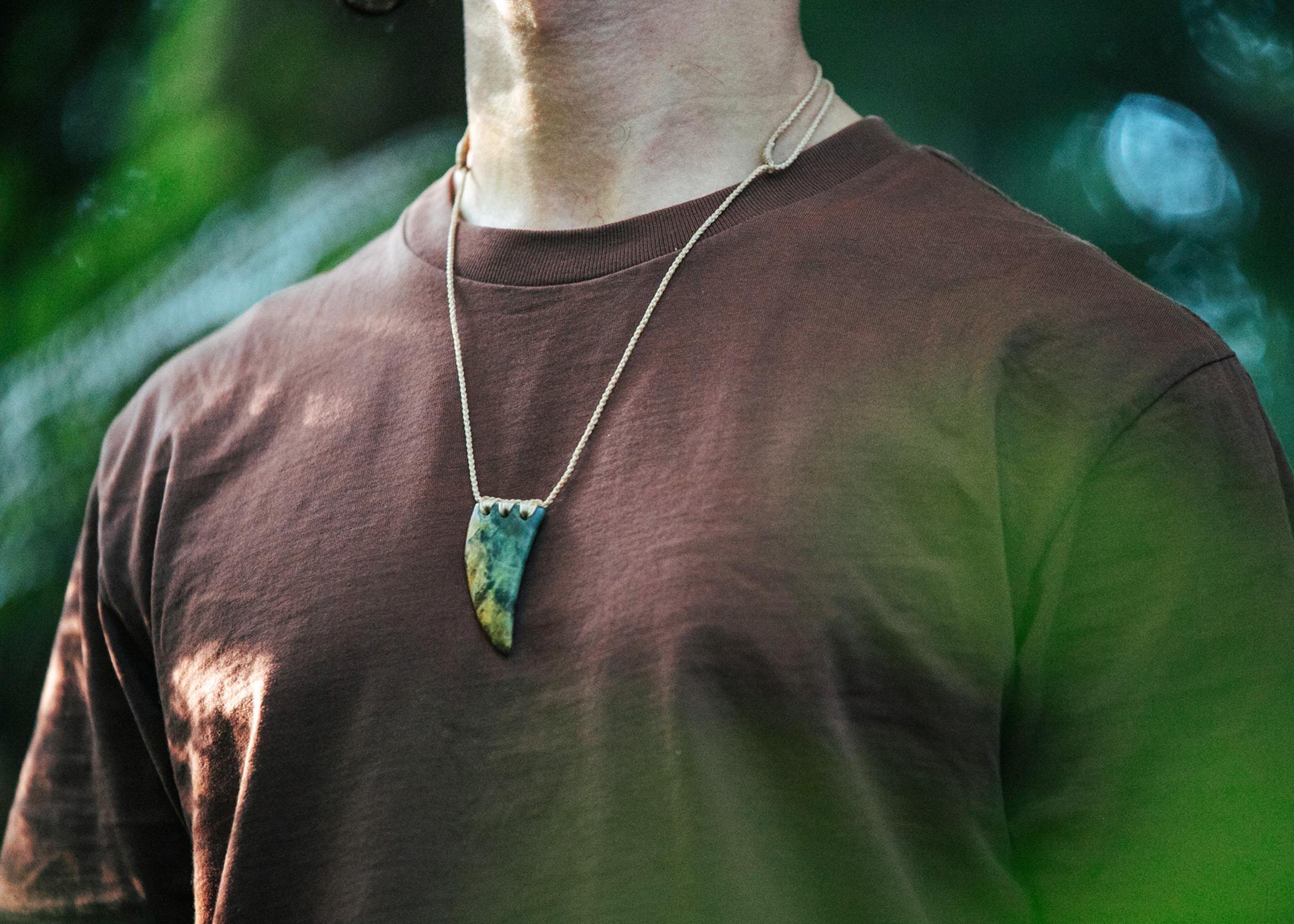 man with brown t shirt wearing pounamu tooth