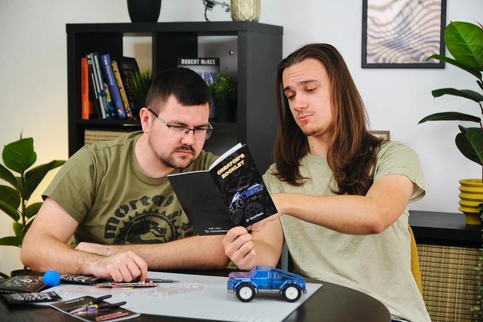 Two men reading Wheelson 2.0 booklet in a living room.