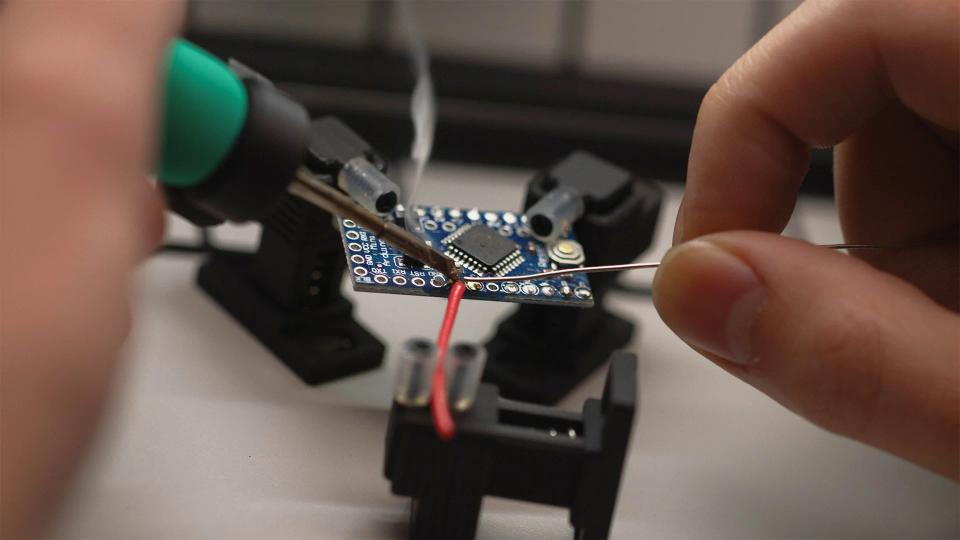 A person soldering with SOLDR Deluxe soldering kit.
