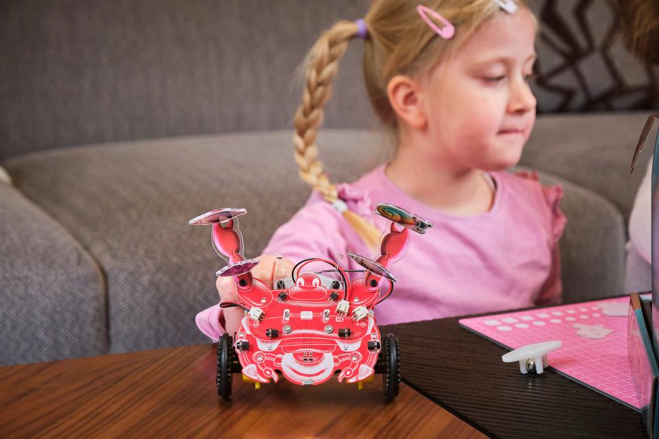A girl playing with CircuitMess Dusty at a table