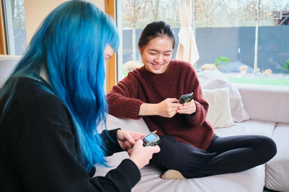 Two women on a couch using CircuitMess Chatter to communicate