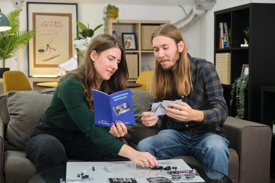 A man and a woman assembling CircuitMess Jay-D 2.0 and Synthia 2.0 in a living room.