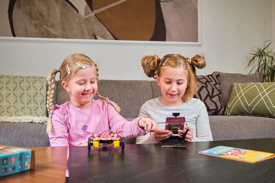 Two girls playing with CircuitMess Dusty at a table