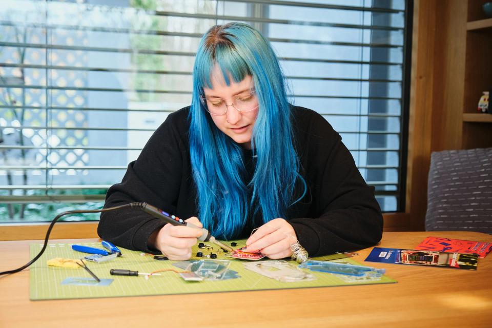 A woman soldering iron parts onto CircuitMess ByteBoi