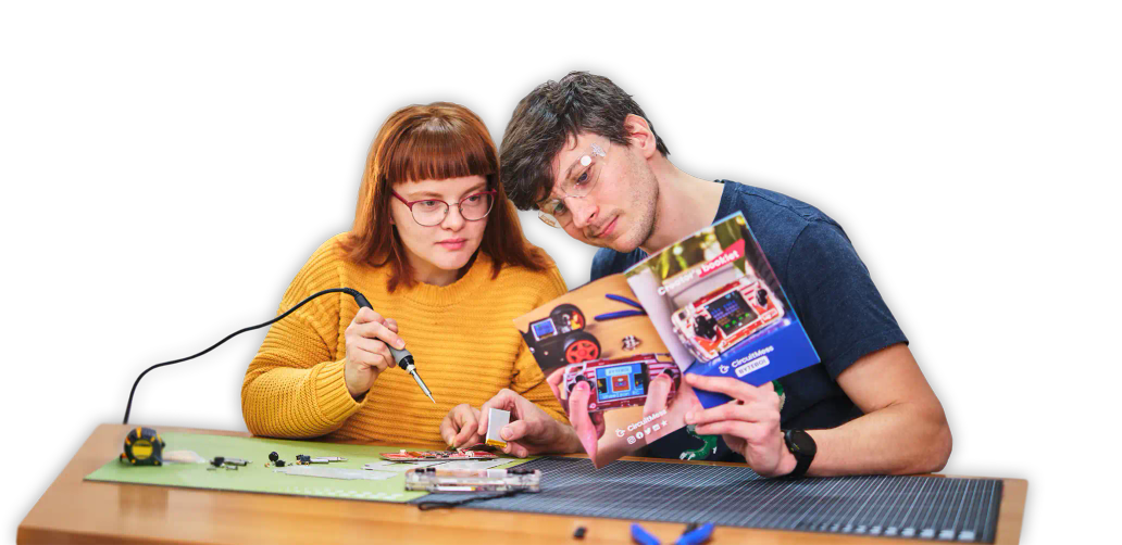 Two people using soldering tools to assemble CircuitMess ByteBoi