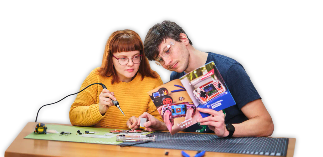 Two people using soldering tools to assemble CircuitMess ByteBoi