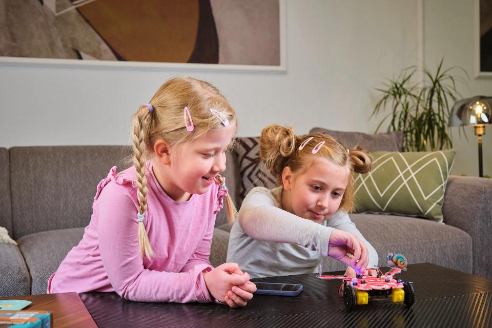Two girls playing with CircuitMess Dusty on a table