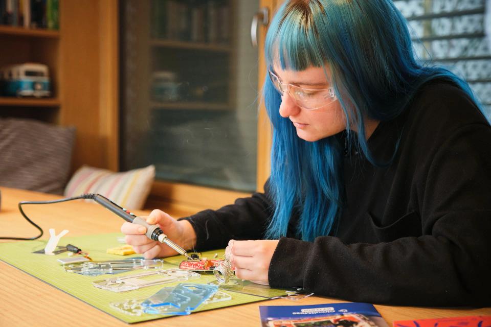 A woman soldering iron parts to CircuitMess ByteBoi