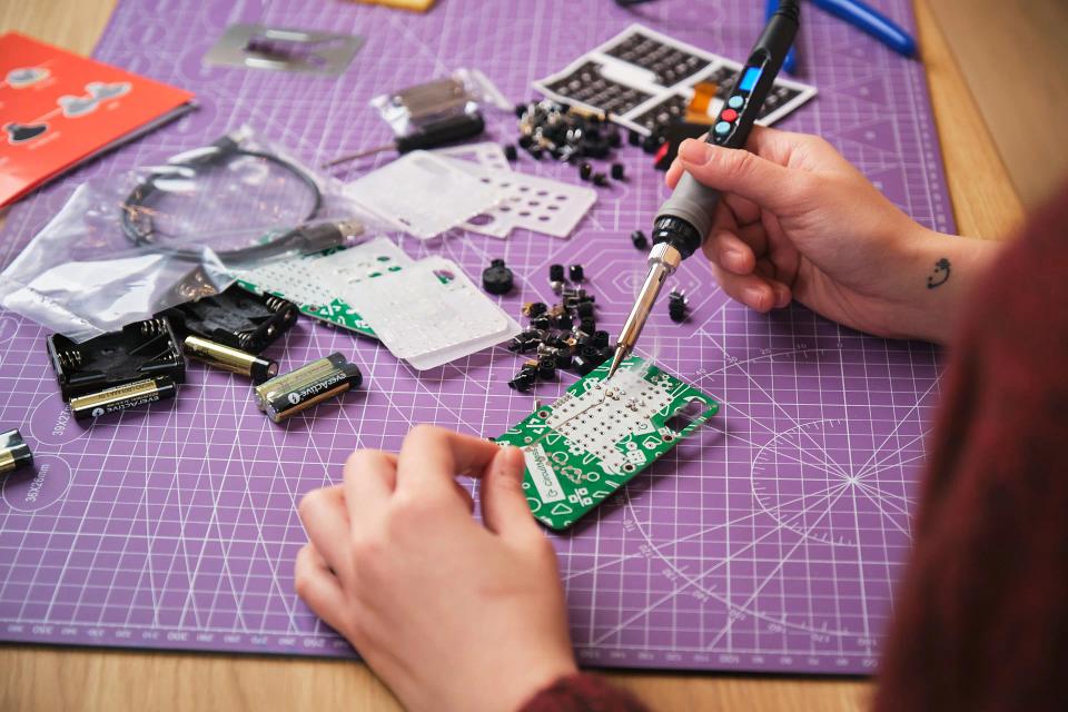 A person using soldering tools to assembled CircuitMess Chatter on a Silicone Work Mat