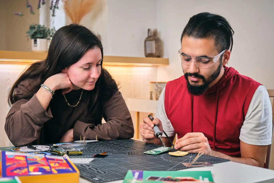 A woman and man using soldering tools to assemble CircuitMess Chatter