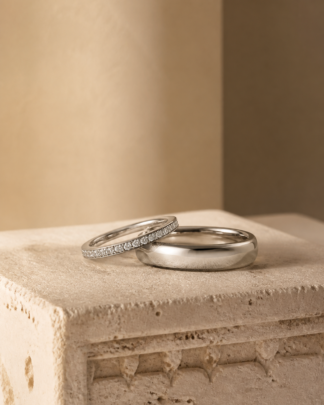 Editorial photograph of a polished wedding band and a diamond-set band on pale stone