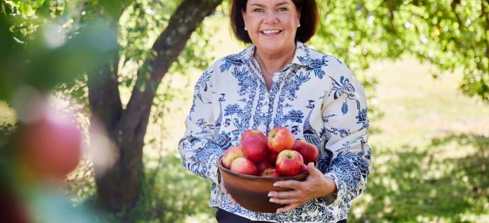 Sissel Brustad under et epletre med en kurv nyplukkede epler