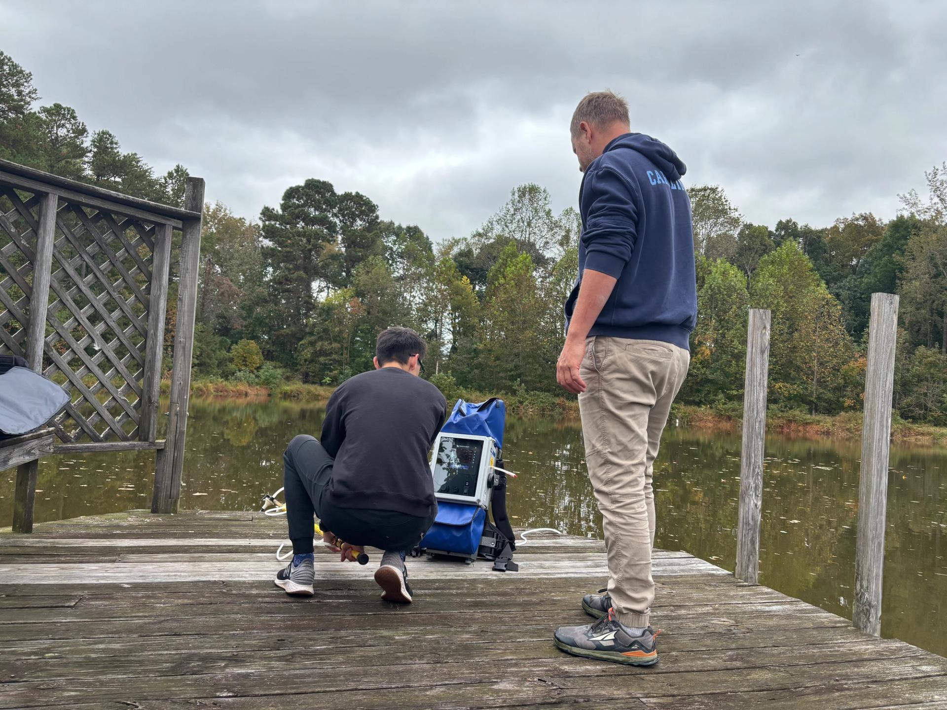 Researchers get a water sample while standing on a wooden boardwalk.