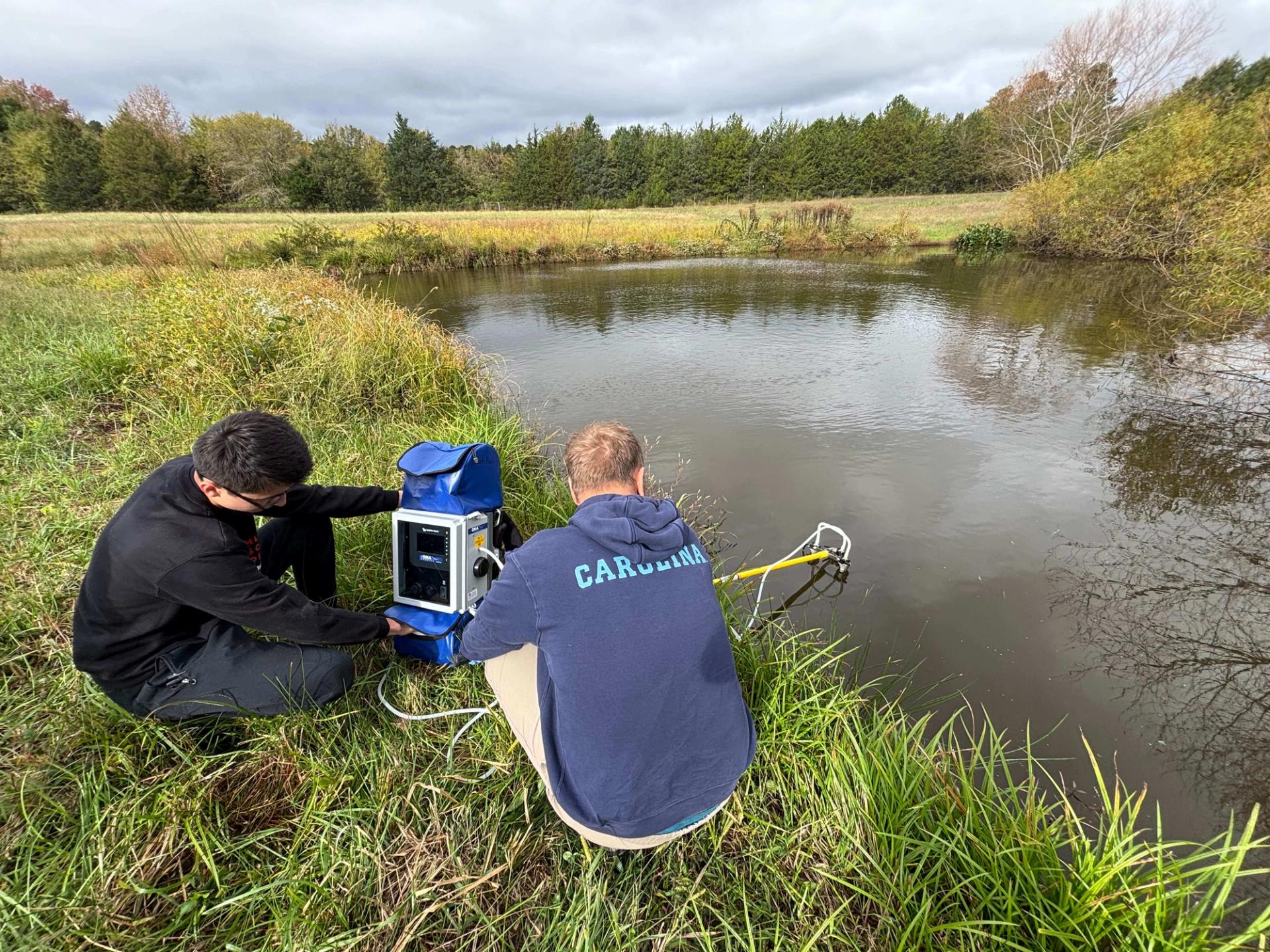 One researcher gets a water sample while the other researcher monitors their equipment.