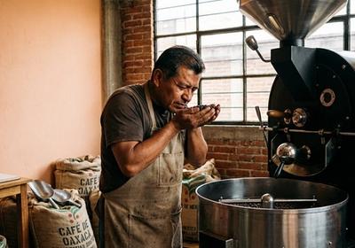 Torréfacteur surveillant attentivement les grains dans une machine à torréfier moderne, avec du café fraîchement torréfié dans le plateau de refroidissement dégageant une fumée aromatique