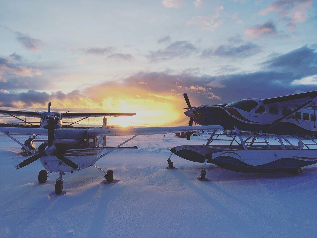 two aircrafts landed on the snow with the sunset in the background.