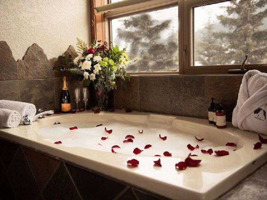 Flower float on a bubble bath with towels, flowers, and wine nearby.